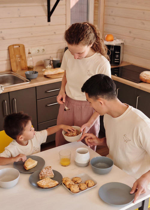 A family of three shares a meal, wearing matching cream-colored t-shirts
